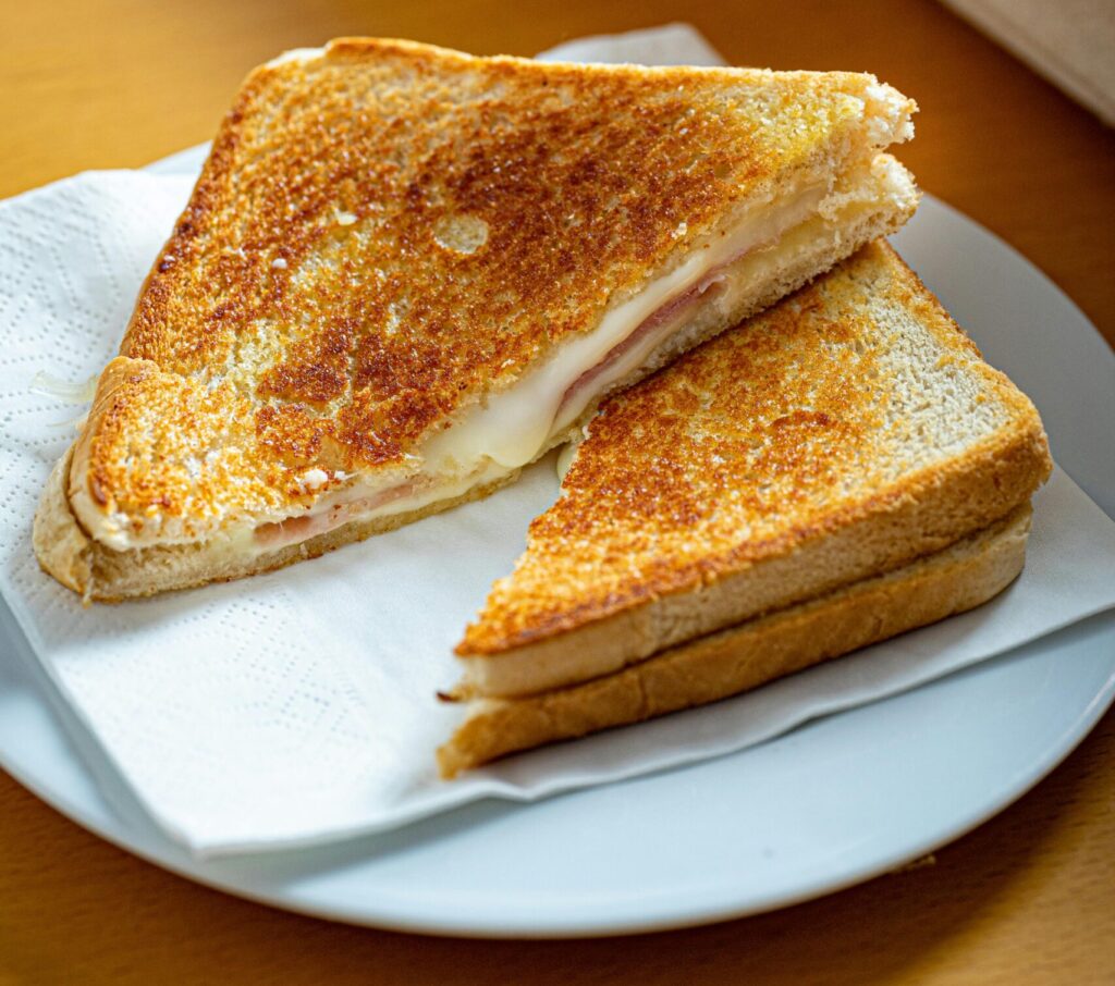 Golden brown grilled cheese sandwich on a white plate with napkin.